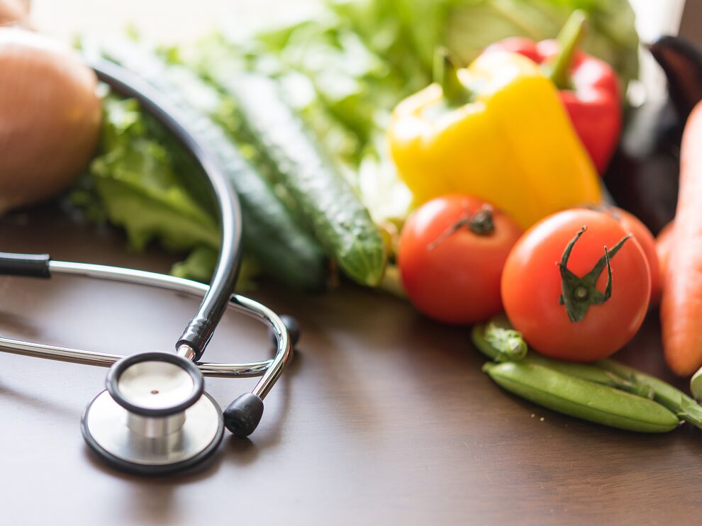 野菜と聴診器が置かれた写真。栄養と健康をイメージした構図