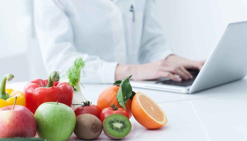 果物とパソコンで作業する医療従事者の写真。栄養指導をイメージ