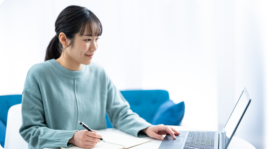ノートにメモを取りながらノートパソコンでオンライン学習をする女性